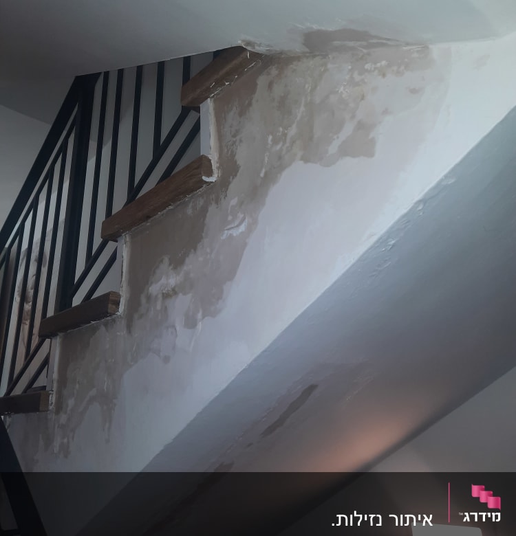 כתמי רטיבות על קיר מדרגות מתחת למעקה מתכת